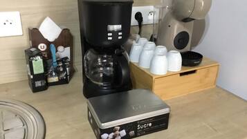 A kitchen area with a coffee maker, a box of sugar, and a set of white cups on a wooden counter.