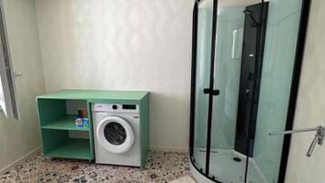 Une petite salle de bain équipée d’un lave-linge, d’une cabine de douche en verre et de carreaux de sol à motifs.