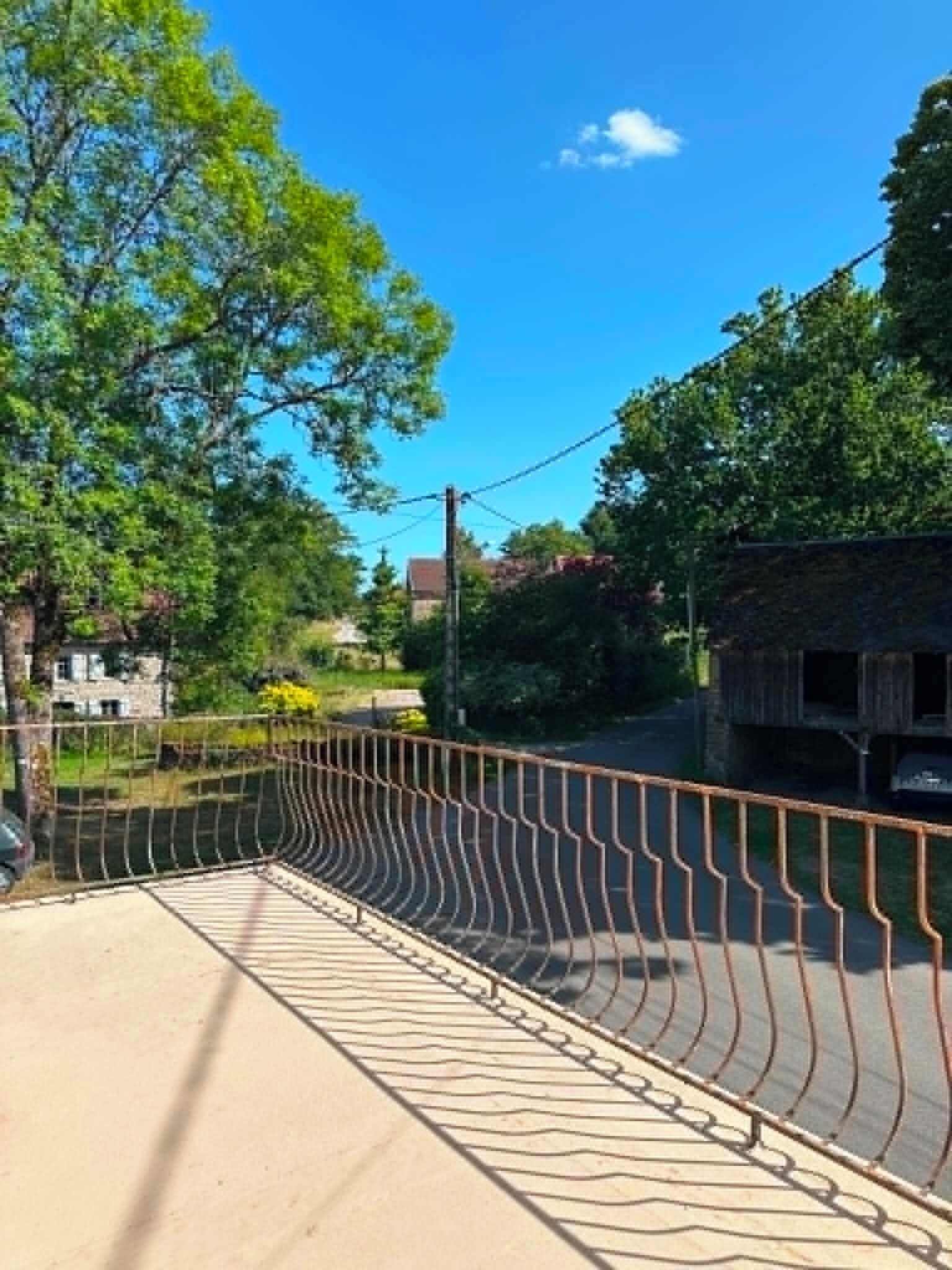 Une clôture en métal avec un sommet incurvé, un chemin pavé et des arbres en arrière-plan.