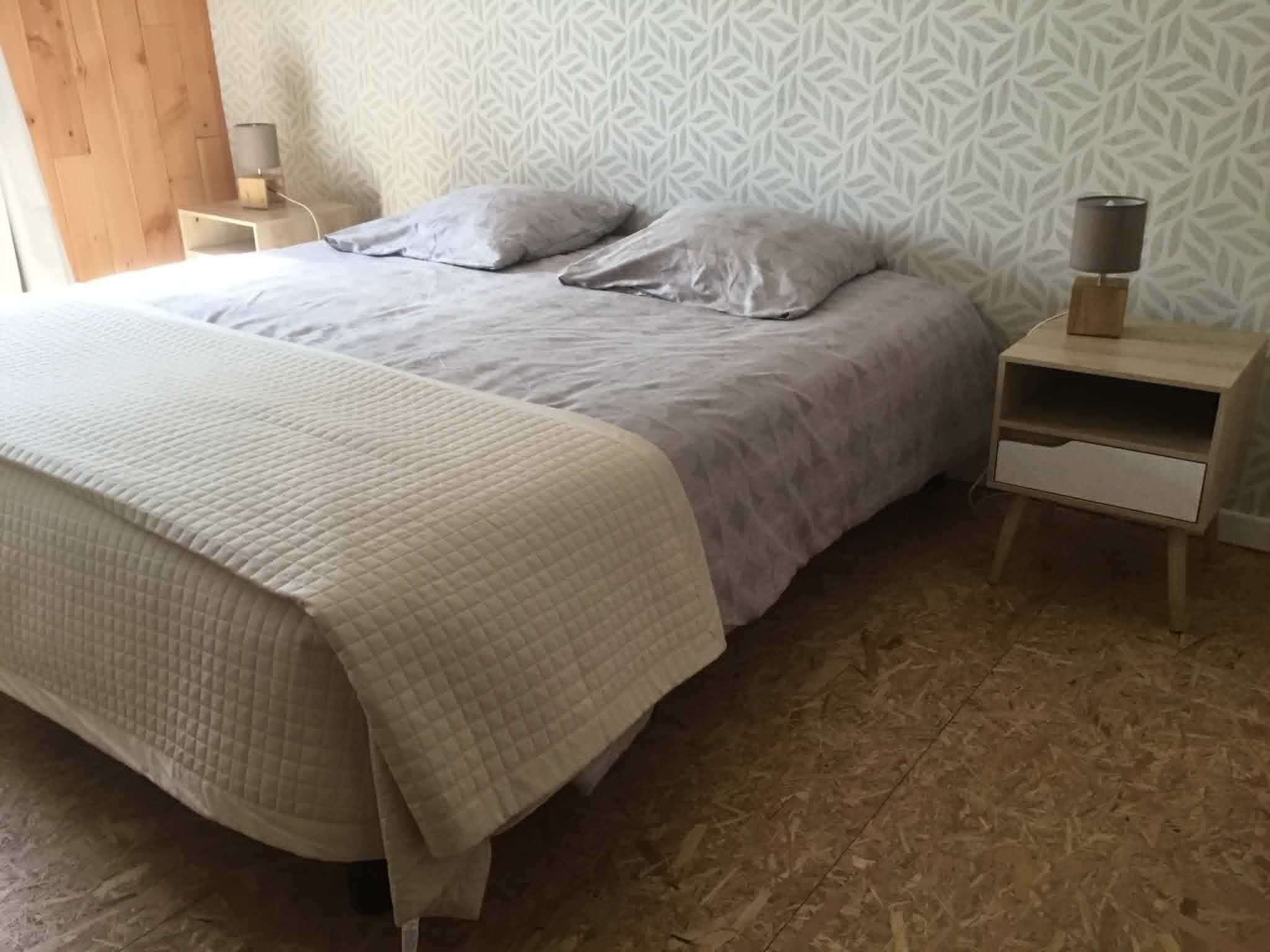 Uma cama com edredom acolchoado, duas almofadas e uma mesa de cabeceira com abajur.