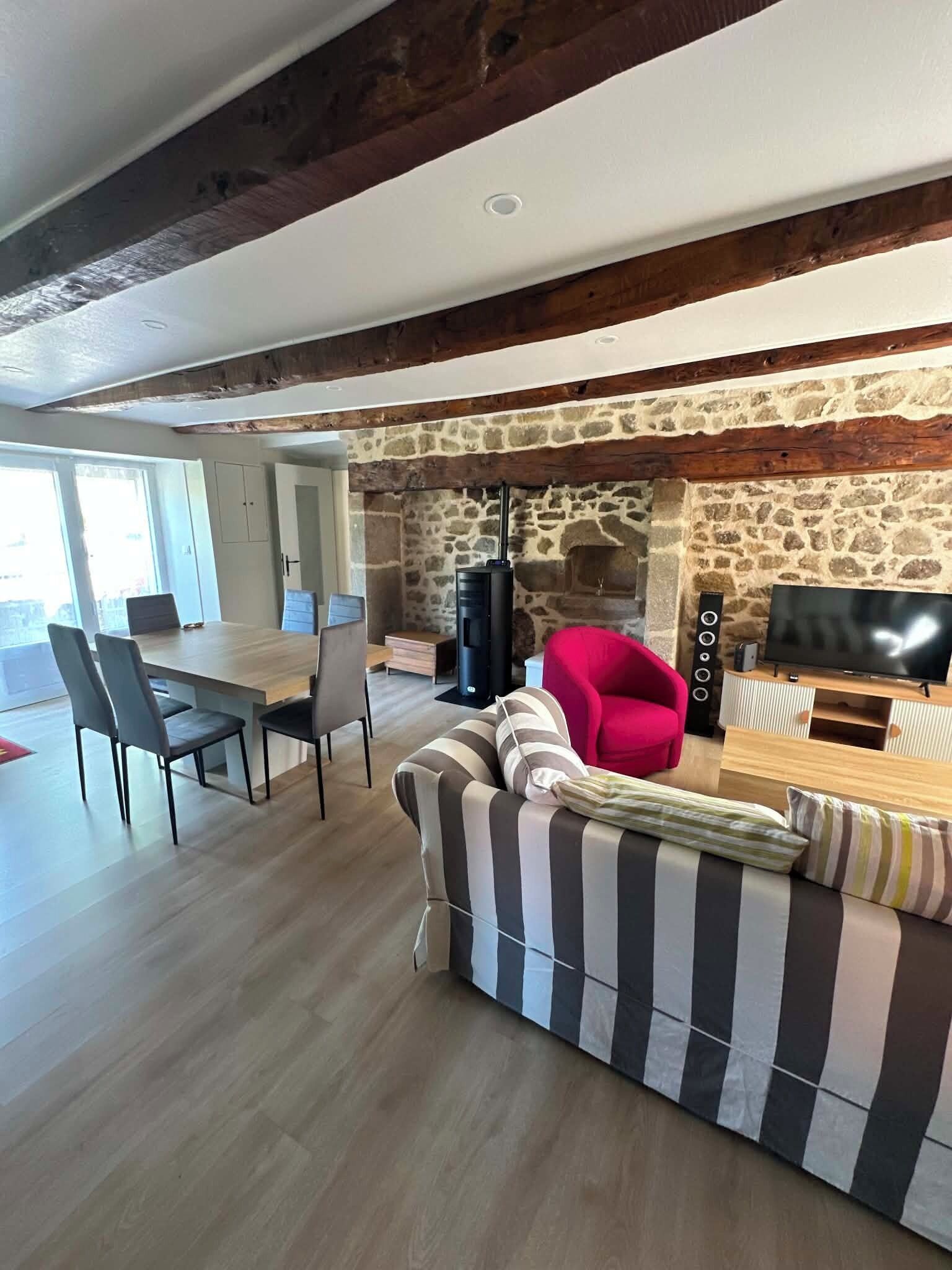 Un salon moderne avec une cheminée en pierre, un canapé, un fauteuil rouge, une table à manger avec des chaises et un téléviseur.