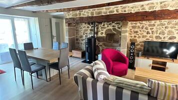 Un salon moderne avec une cheminée en pierre, un canapé, un fauteuil rouge, une table à manger avec des chaises et un téléviseur.