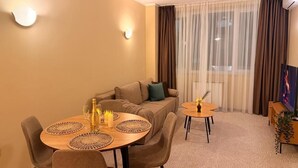 A living room with a sofa, two round tables, a TV, and a large window with curtains. - Hotel NIRA (Sofia)