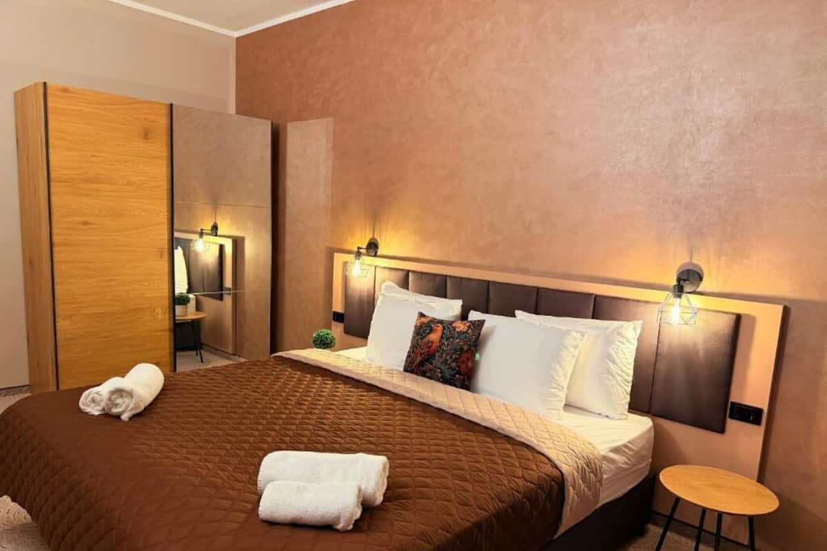 Una habitación de hotel moderna con una cama grande, lámparas de noche, una mesita y un armario.