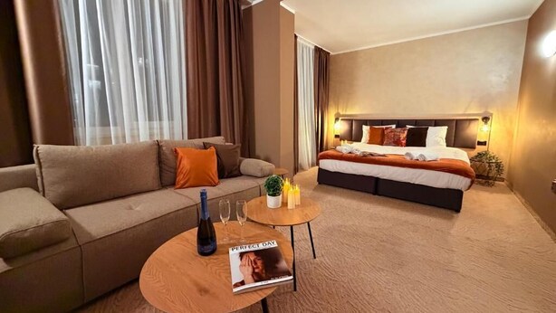 A hotel room with a sofa, a bed, a small table with a magazine, and a bottle. - Hotel NIRA (Sofia)