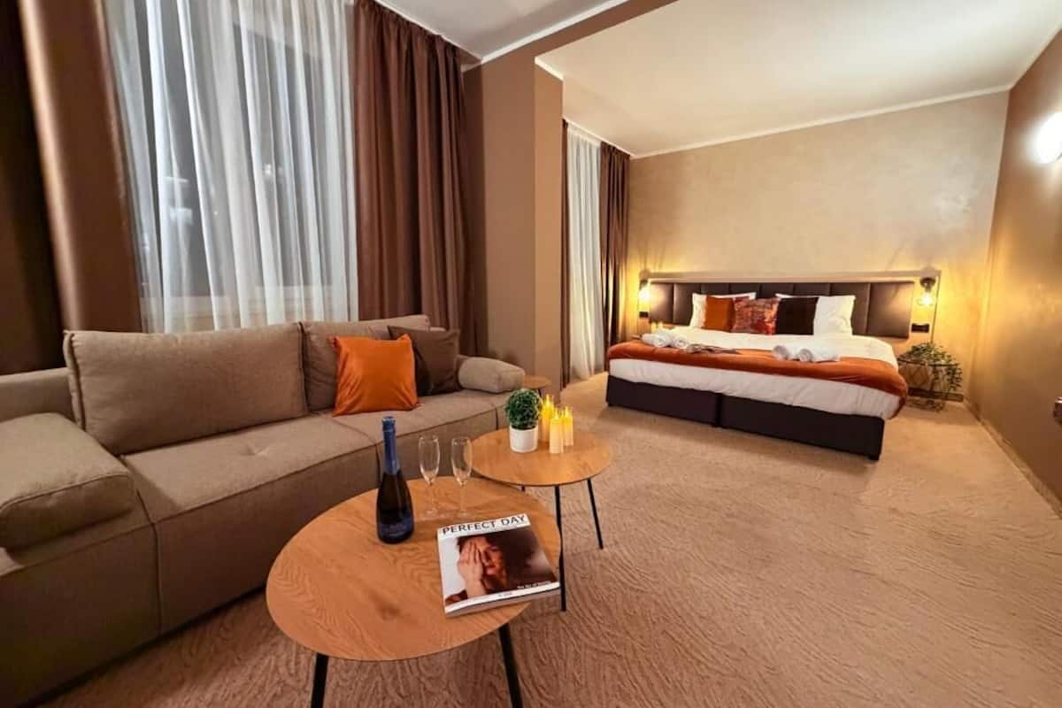 Habitación de hotel con sofá, cama, una mesita con una revista y una botella.