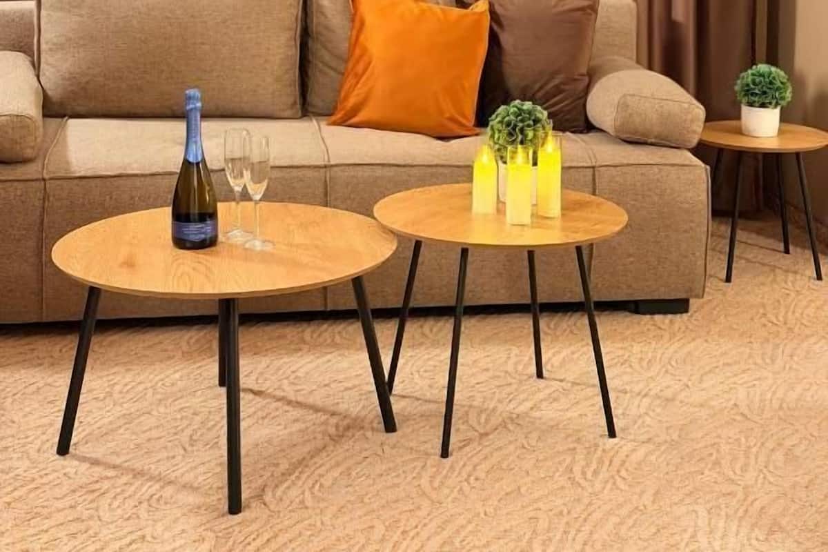 Un salón con sofá, dos mesas redondas, una botella de vino y una planta pequeña.