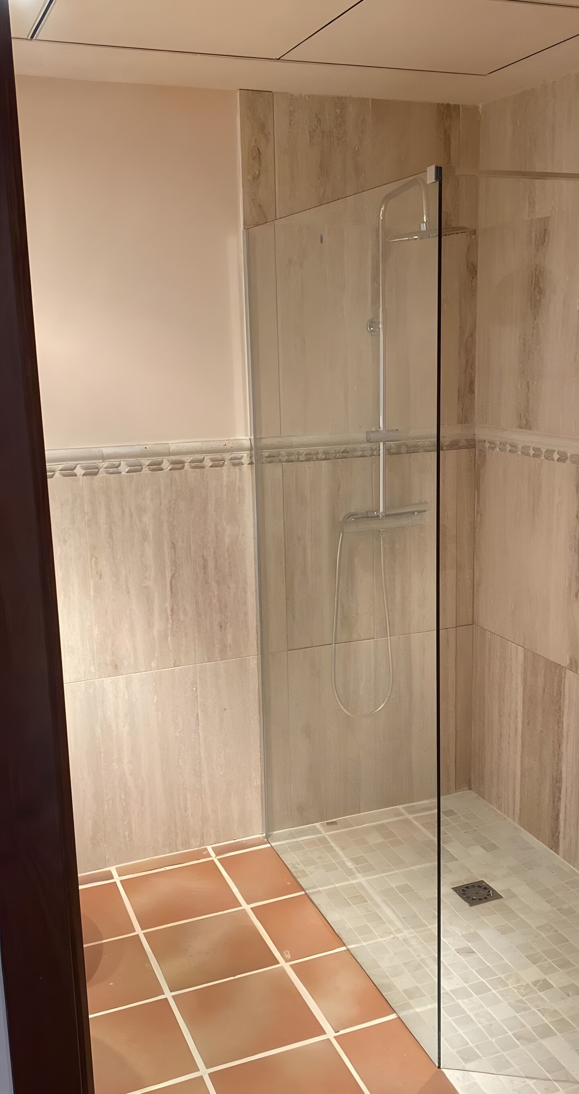 A shower with a glass door, tiled walls, and a tiled floor.