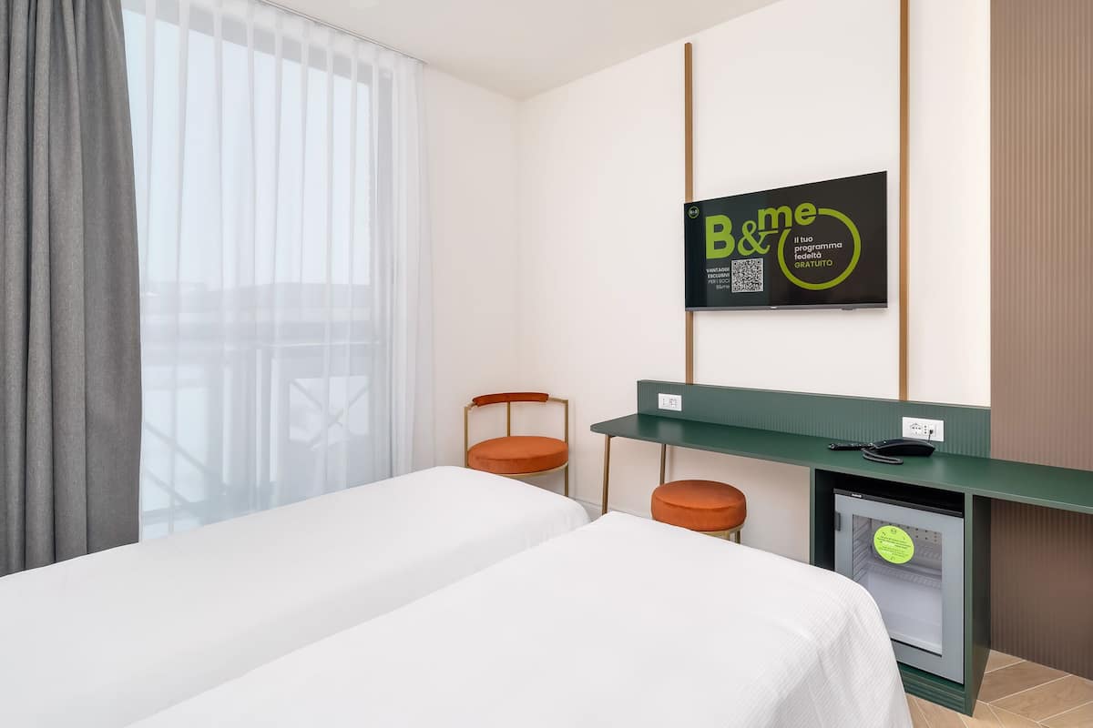 Ein Hotelzimmer mit einem Bett, einem Schreibtisch, zwei Stühlen, einem Fernseher und einem Kühlschrank.