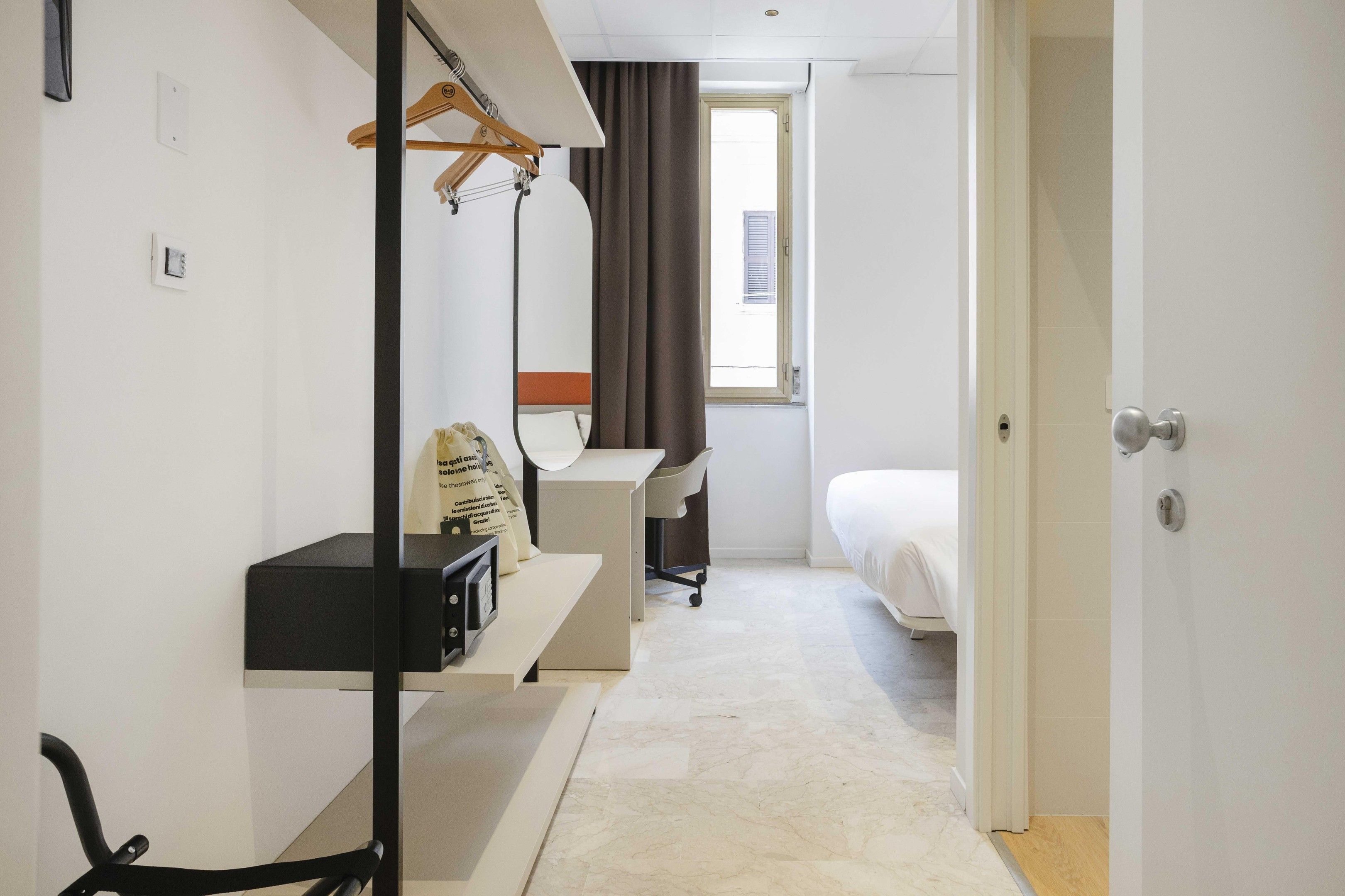 Une chambre d’hôtel avec un lit, un bureau, une chaise, un miroir et une fenêtre.