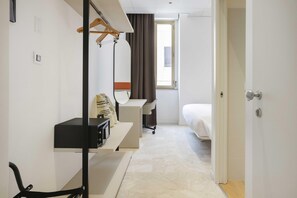Una habitación de hotel con una cama, un escritorio, una silla, un espejo y una ventana.