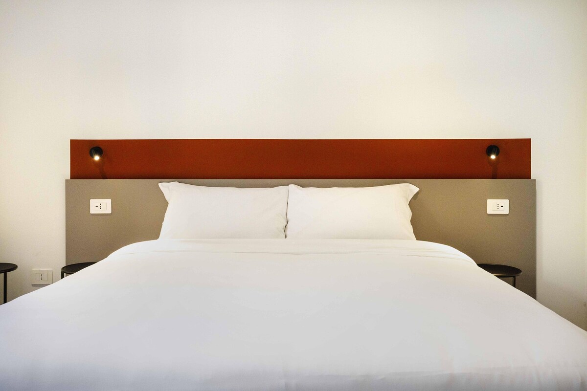 Een hotelkamer met een bed, twee nachtkastjes en een wandlamp.