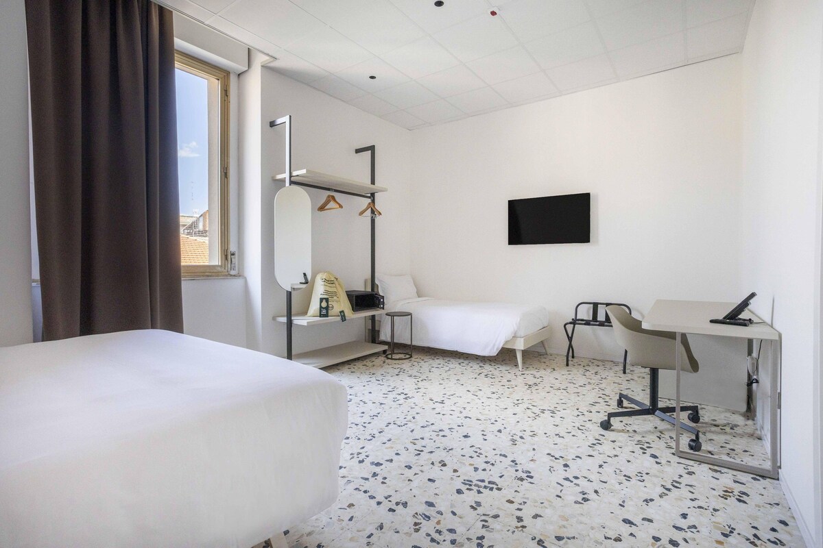 Habitación de hotel con dos camas, un escritorio, una silla, un televisor y una ventana con cortinas.