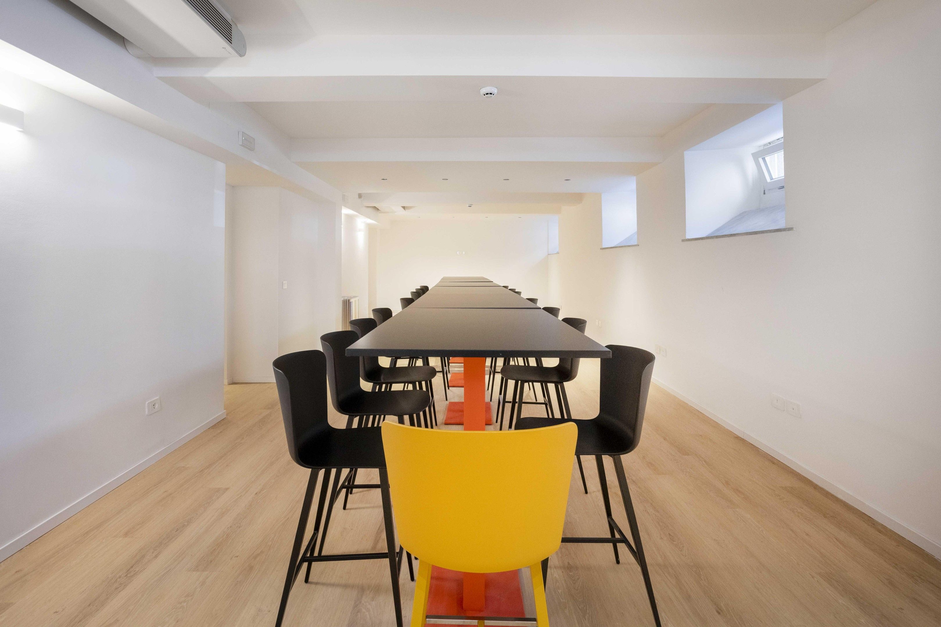 Una sala conferenze con un lungo tavolo, sedie nere e una sedia gialla.
