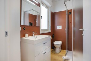 Een badkamer met een wit wastafelmeubel, een spiegel, een toilet en een douchecabine met glazen wanden.