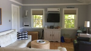 Ein Wohnzimmer mit einer Couch, einem Hocker und einem Fernseher an der Wand.