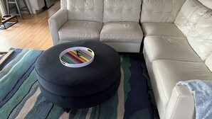 Ein modulares Sofa, ein schwarzer Hocker mit einem bunten Tablett und ein gestreifter Teppich im Wohnzimmer.
