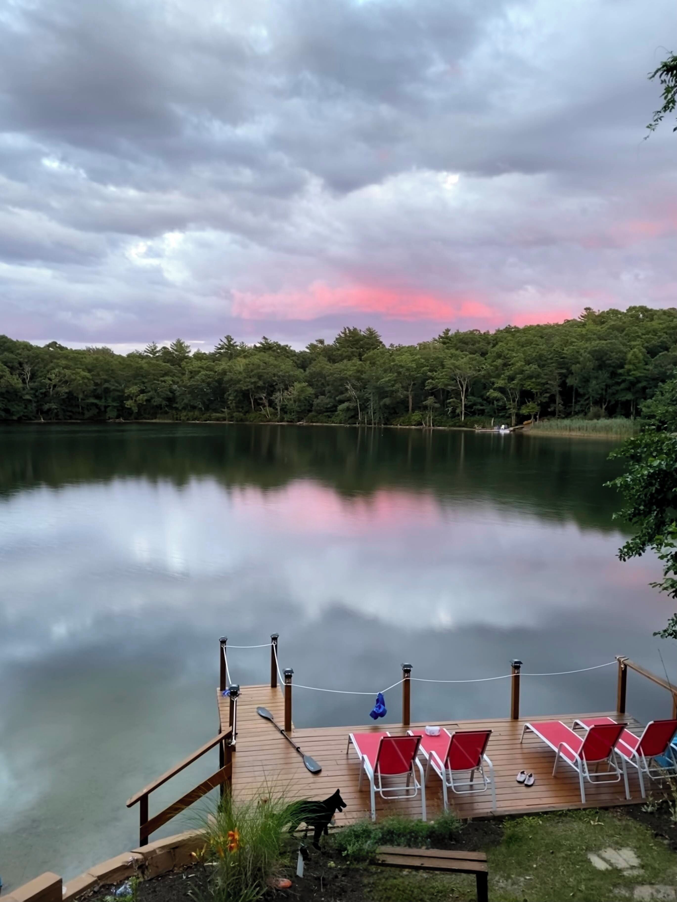 Ein ruhiger See mit einer Anlegestelle, Stand-Up-Paddles und roten Stühlen.