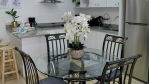 Een moderne keuken met witte kasten, een roestvrijstalen koelkast en een glazen eettafel met stoelen.
