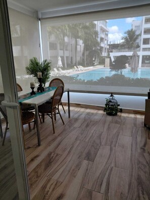 Ein Balkon mit Esstisch, Stühlen, einem Blumentopf und Blick auf einen Pool und Gebäude.