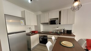 Una cocina moderna con armarios blancos, electrodomésticos de acero inoxidable, una mesa de comedor de madera y una lámpara colgante.