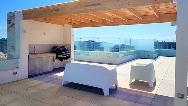 Una terraza en la azotea con una pérgola de madera, un banco blanco, una mesita blanca y una barandilla de cristal con vistas a un paisaje urbano.