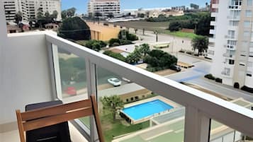 Uma varanda com vista para uma piscina, uma mesa com uma cadeira e um vaso de flores.