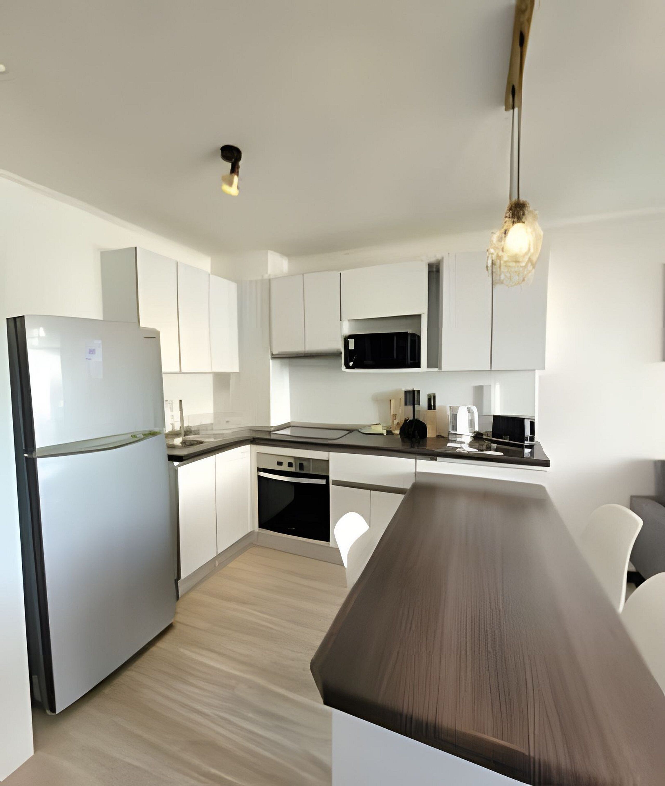 A modern kitchen with white cabinetry, a built-in oven, a microwave, and a wooden countertop.