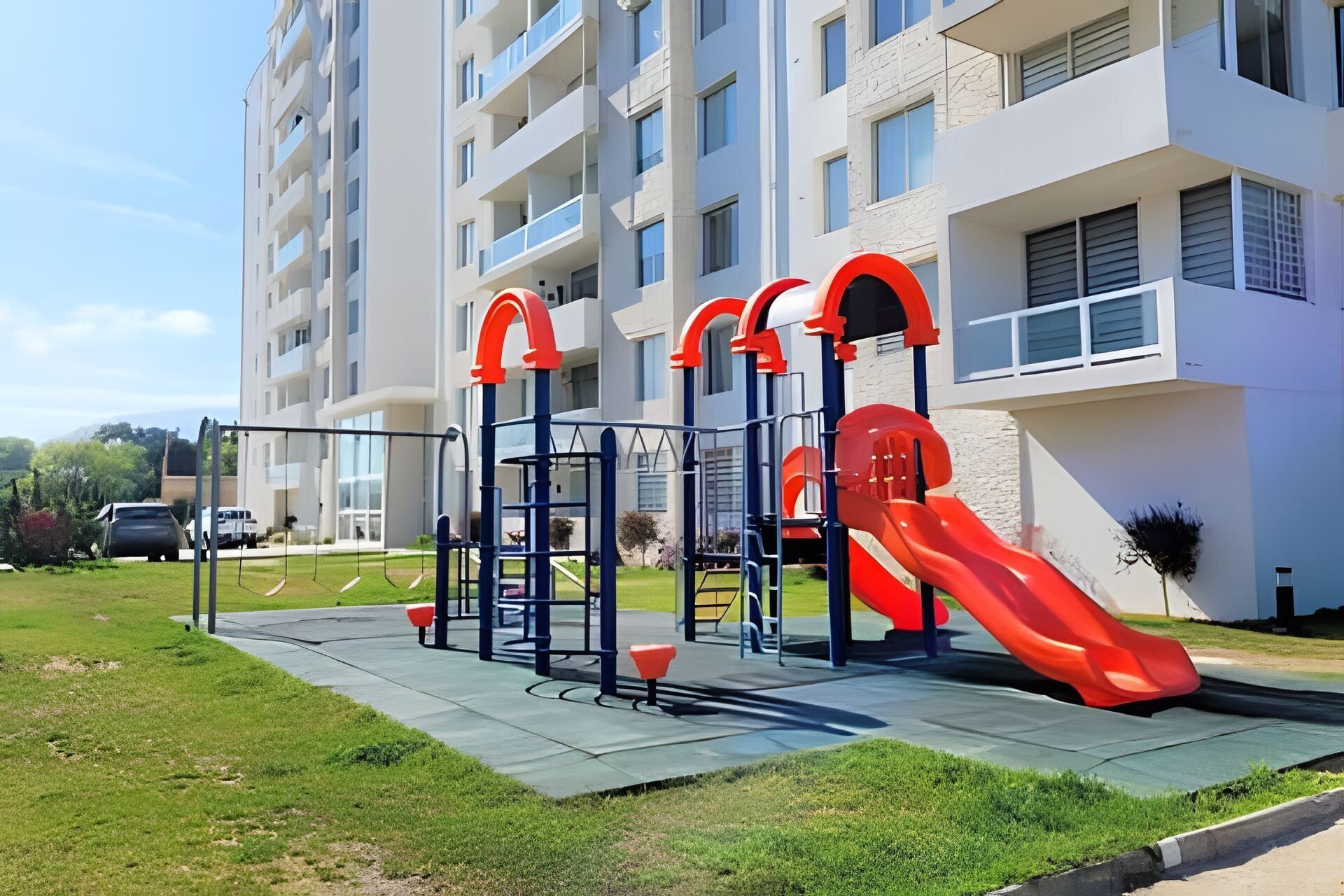 Un terrain de jeux avec un toboggan et des structures d’escalade, situé devant un immeuble d’appartements moderne.