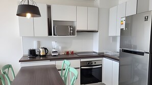Ett modernt kök med vita skåp, vitvaror i rostfritt stål, ett matbord i trä och stolar i turkos.