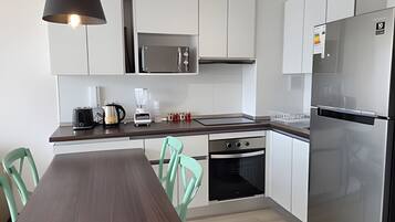 A modern kitchen with white cabinets, stainless steel appliances, a wooden dining table, and teal chairs.