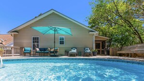 A swimming pool with a wooden deck, a covered seating area, and a house in the background. - Tracie's Oasis - Pool/fenced/beach walkable! (Oak Island)