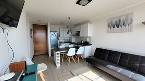 Una cocina moderna con armarios blancos, encimera negra y comedor con sofá negro y sillas blancas.