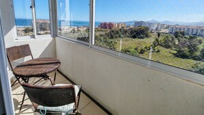 Un balcón con sillas de mimbre, vista al mar y edificios a lo lejos.