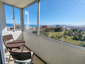 Ein Balkon mit Korbstühlen, Blick auf das Meer und Gebäude in der Ferne.
