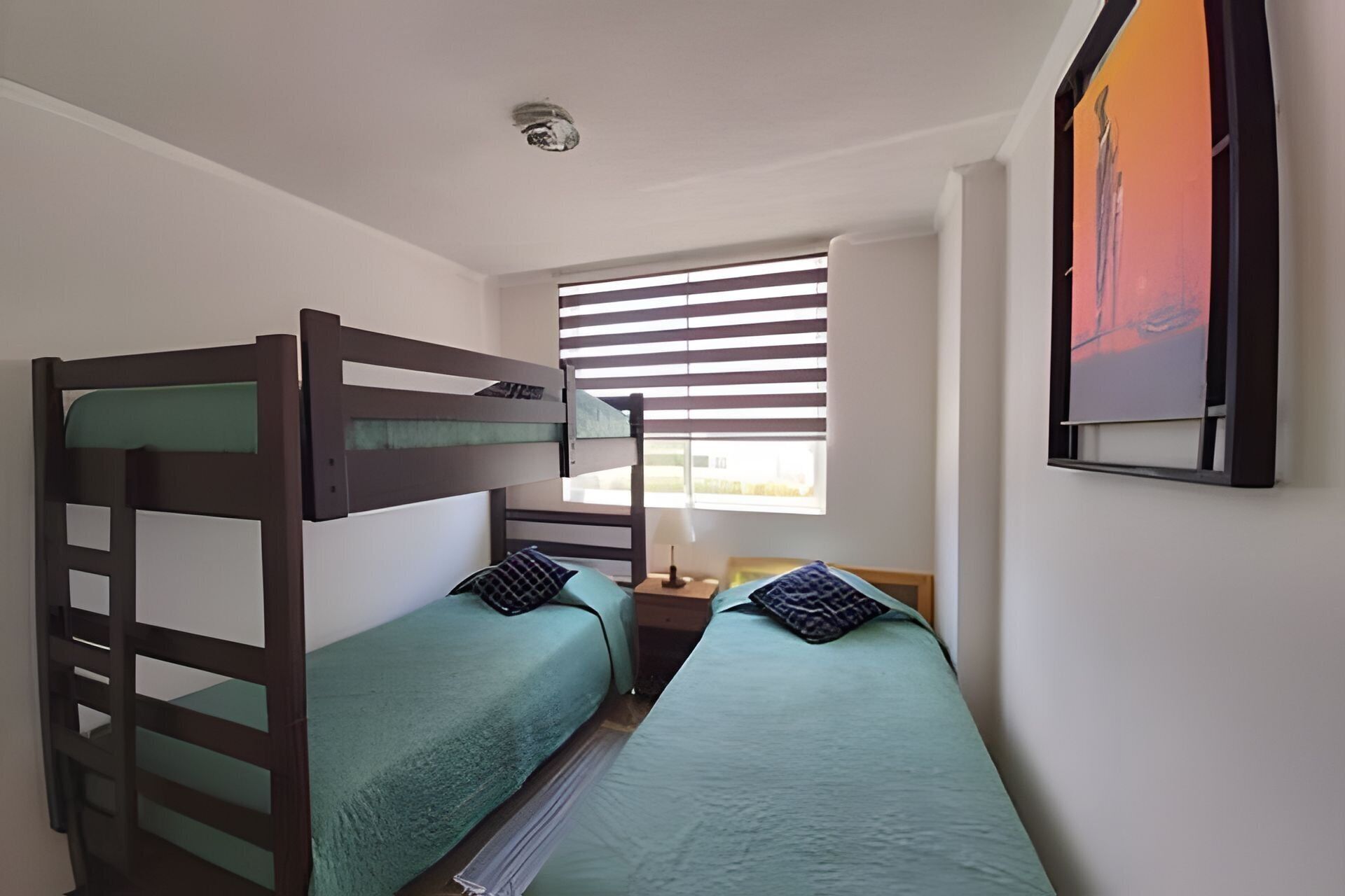 A room with two bunk beds, a small table with a lamp, and a window with blinds.