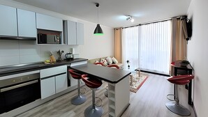 Une cuisine moderne avec des meubles blancs, un îlot central doté de tabourets, une table à manger et un ventilateur de plafond.