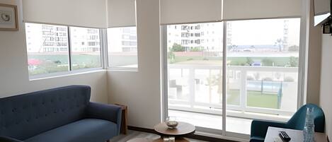 A modern living room with a sofa, two small round tables, and large windows offering a view of a residential area.
