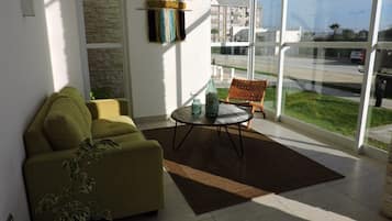 A living room with a sofa, a coffee table, a rug, and a view through large windows.