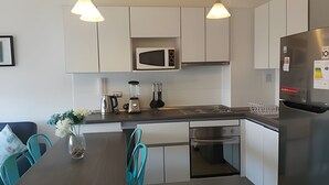 Een moderne keuken met witte kastjes, een magnetron, een koelkast, een fornuis en een eethoek met teal-kleurige stoelen en een vaas met bloemen.