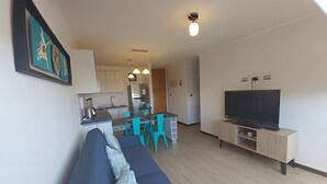 Een moderne woonkamer met een bank, een televisie en een keuken op de achtergrond.