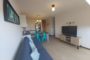 Ein modernes Wohnzimmer mit einer Couch, einem Fernseher und einer Küche im Hintergrund.