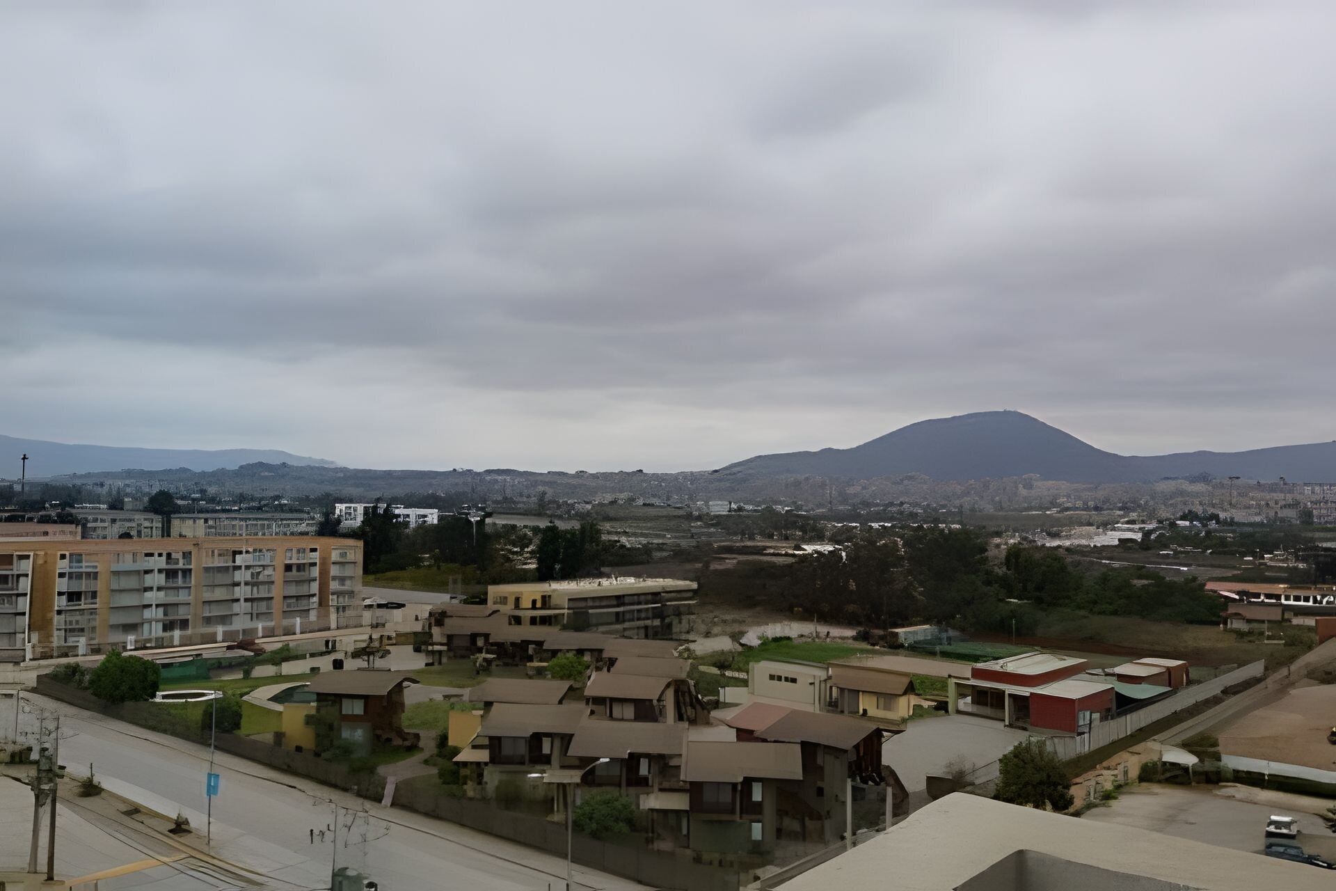 Zona residencial con una mezcla de viviendas modernas y tradicionales, una montaña destacada al fondo y cielo despejado.