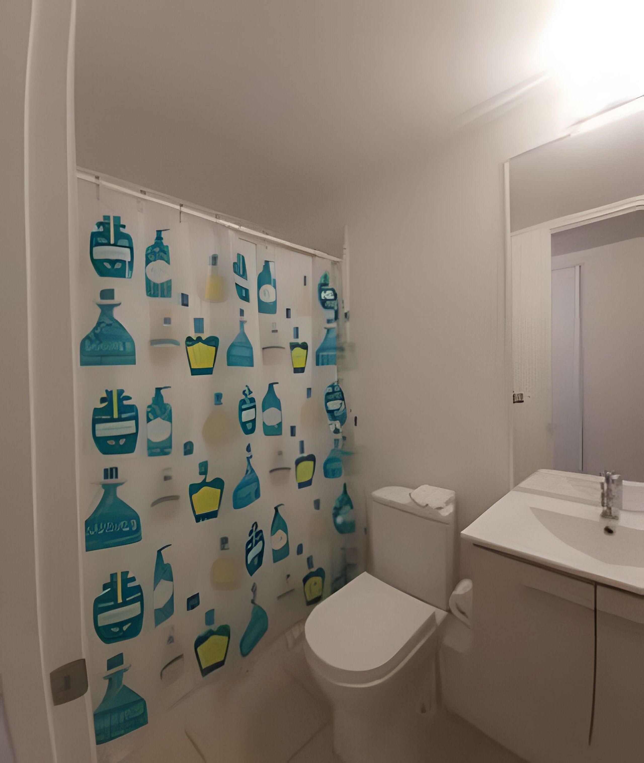 A bathroom with a toilet, a sink, and a shower curtain with a pattern of various shapes and sizes.