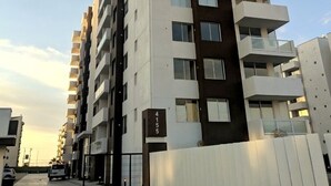 Un edificio residencial de varios pisos con balcones, una entrada con reja y cielo despejado.