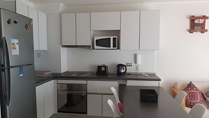Una cocina moderna con armarios blancos, microondas, cafetera y refrigerador.