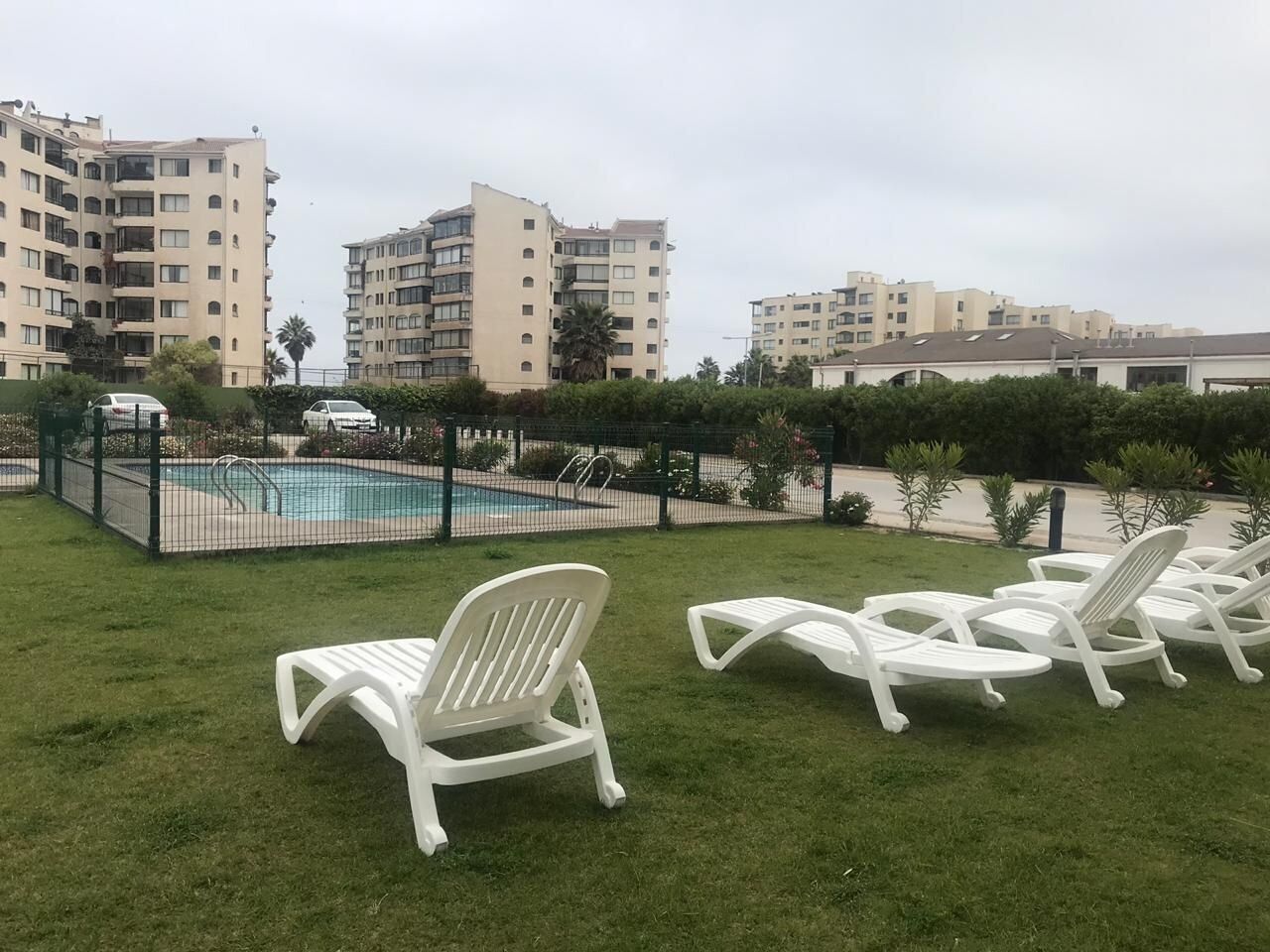 Uma área de piscina com espreguiçadeiras, piscina cercada e edifícios altos ao fundo.