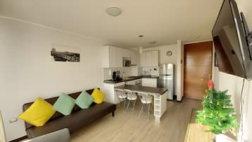A compact living space with a kitchenette, a sofa with cushions, a dining area, and a television.
