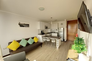 Ein kompakter Wohnbereich mit Küchenzeile, einer Couch mit Kissen, einem Essbereich und einem Fernseher.
