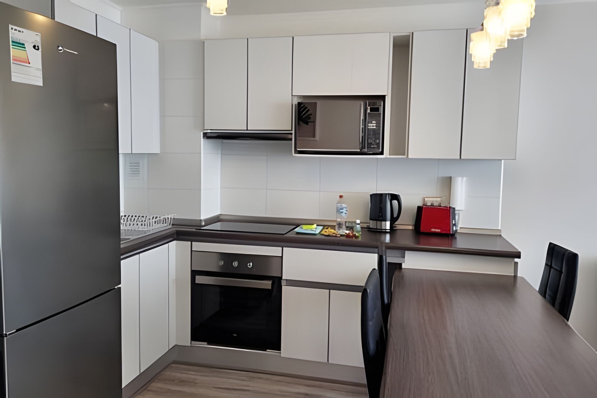 A modern kitchen with a built-in microwave, stainless steel refrigerator, and a wooden dining table.